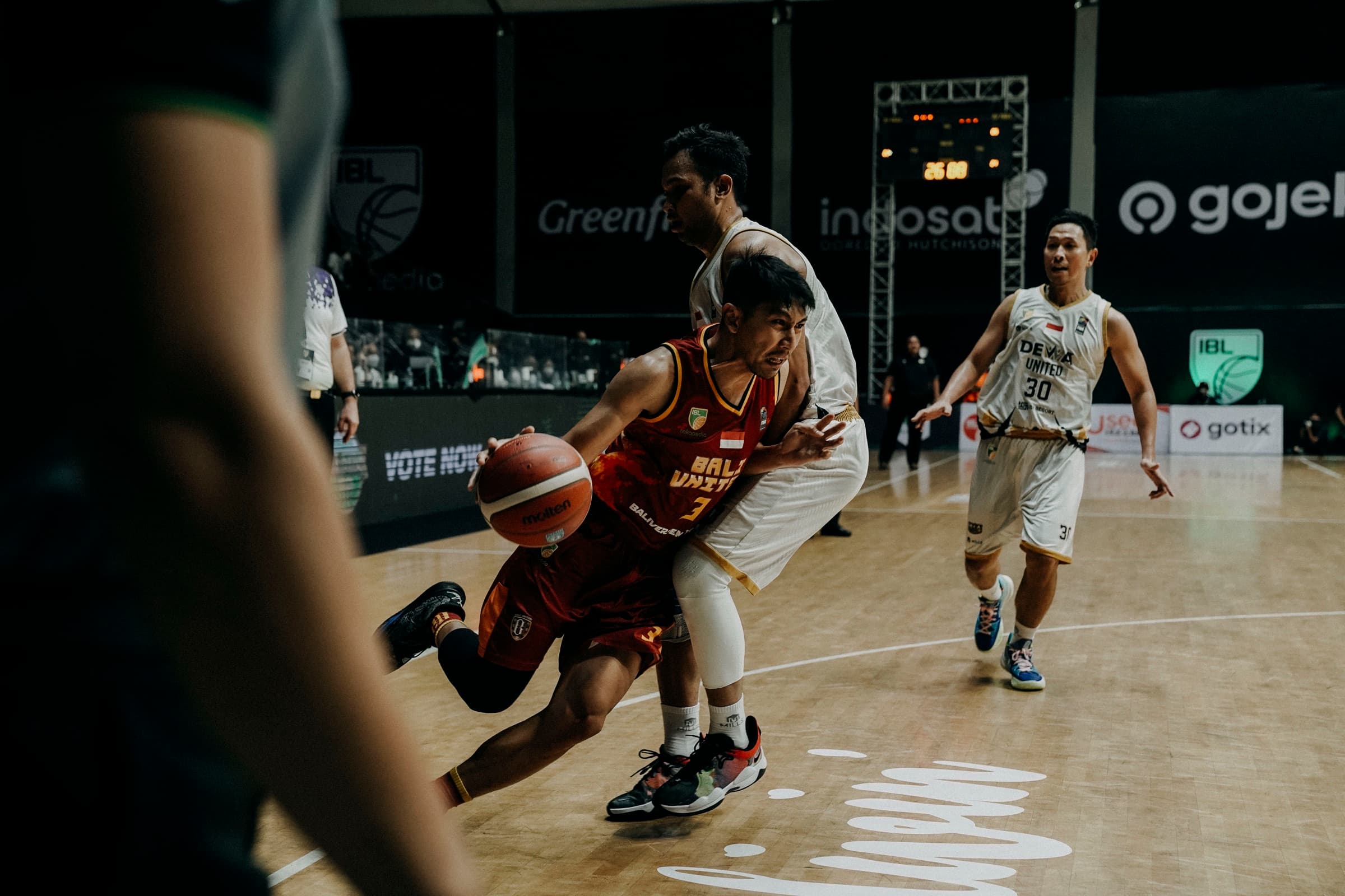 A guard in a dark red Bali United jersey driving past a Dewa United defender during an IBL league game.